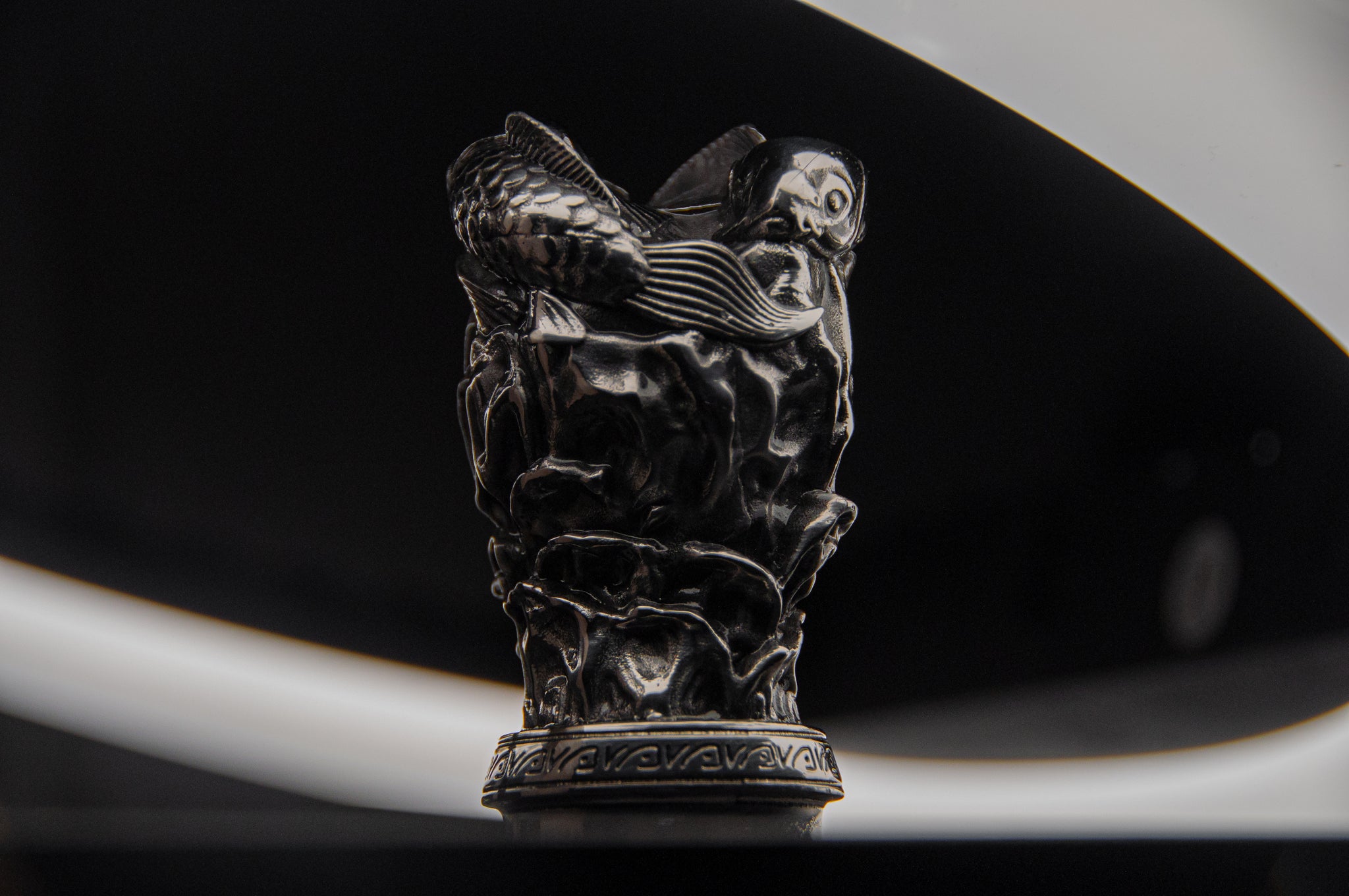 The Twin Koi Fish | Artisan Shift Knob by Incompletegl is an intricately carved metallic object showcasing Japanese heritage, featuring a fish and waves against a dark background accented by white, swirling light.