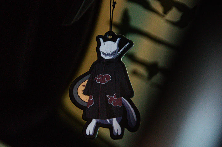 A stylized character pendant from the Naruto Mystery Pack! | Anime Bundle Pack by Incompletegl is displayed against a blurred, dark background. The character wears a black cloak with red cloud patterns and features cat-like traits along with a long tail, capturing the essence of the Naruto-themed aesthetic.