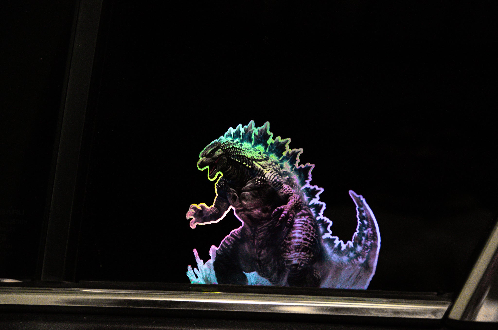 Against a black background, the GODZILLA! | Holo Peeker from Incompletegl showcases a holographic image of a colorful Godzilla, complete with an illuminated dorsal fin. The creature is portrayed in a dynamic pose, giving the illusion of motion. Its colors range from green to purple, creating a glowing effect that evokes the iconic giant monsters of Japanese cinema.