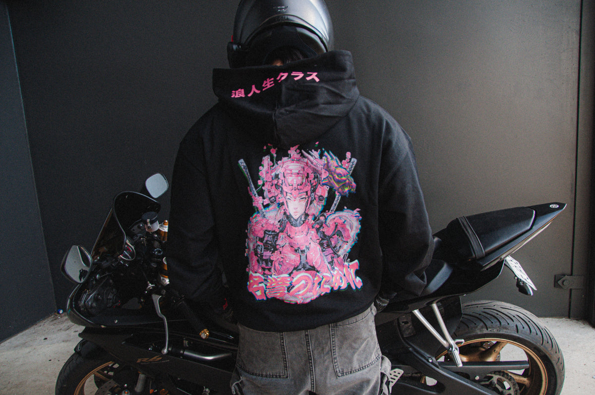 A person wearing an oversized black hoodie from the Incompletegl Mecha Geisha collection, featuring a vibrant and detailed Mecha Geisha design on the back, stands next to a sleek black sports motorcycle. The individual also dons a black helmet, set against a dark and minimalist background.