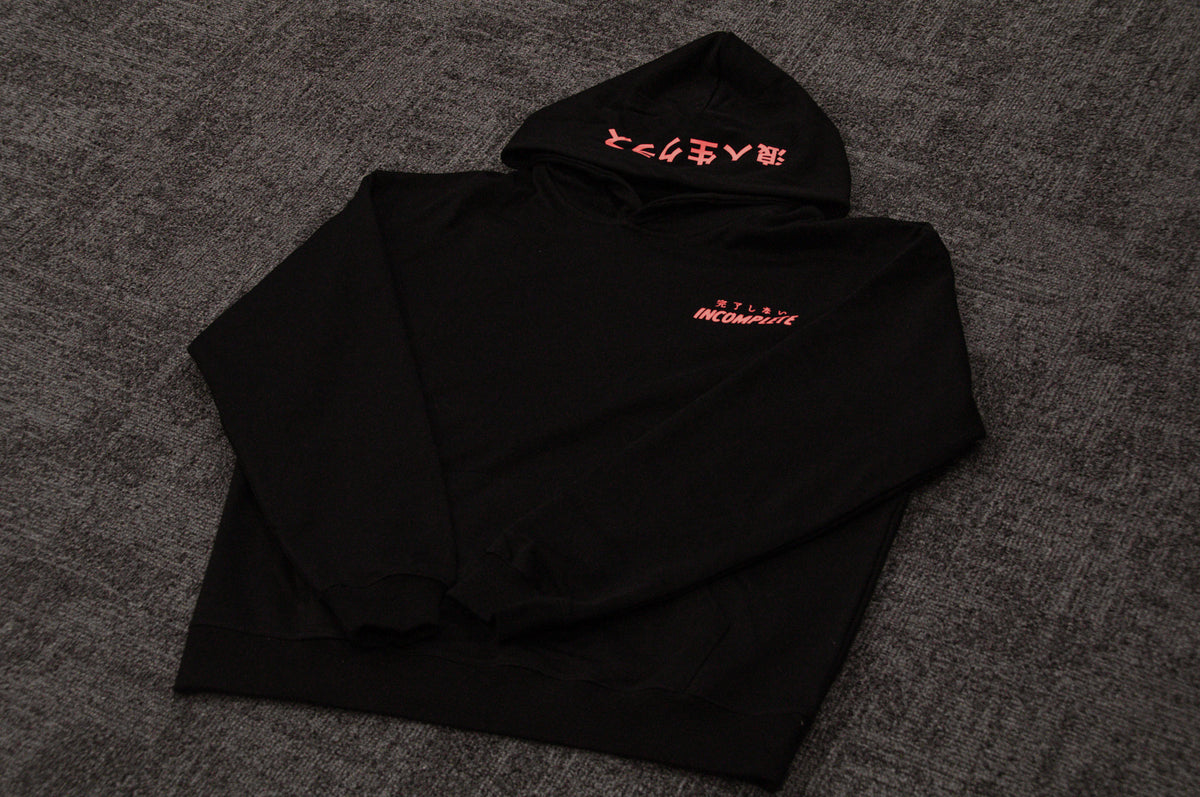 The Mecha Ronin | Oversized Hoodie by Incompletegl, featuring black fabric with striking red text, is showcased on a dark gray carpet to evoke cyberpunk aesthetics. The front displays the words "INCOMPLETE" and "NTLS" in vivid red, while the hood features additional red text in a different language, enhancing its Ronin Class allure.