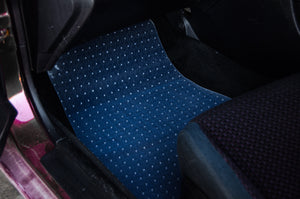 A close-up view of the front passenger floor area of a car reveals it is covered with *Floor Mat Protection!*'s blue, dotted PVC floor mat from *Incompletegl.*, perfectly designed for car interior protection. The edge of the car seat is partially visible to the right, highlighting the custom JDM mat's textured dotted pattern that stands out against the dark surroundings.