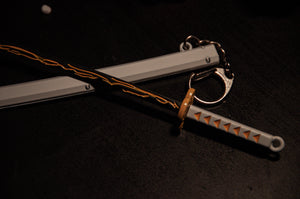 Introducing the Demon Slayer Swords! keychain by Incompletegl— a must-have for anime enthusiasts. This miniature katana features a detailed yellow and black blade with flame-like patterns, elegantly resting on a white sheath complete with a metal keyring. The hilt is white with an intricate yellow guard and orange diamond patterns on the grip. Ideal for fans of Demon Slayer Sword Keychains.