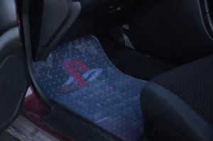 In the front passenger footwell of a vehicle, an Incompletegl Floor Mat Protection! PVC Floor Mat featuring the PlayStation logo and text is displayed. With a black background adorned with blue and white speckles, it is surrounded by partially visible black seats, providing stylish car interior protection.