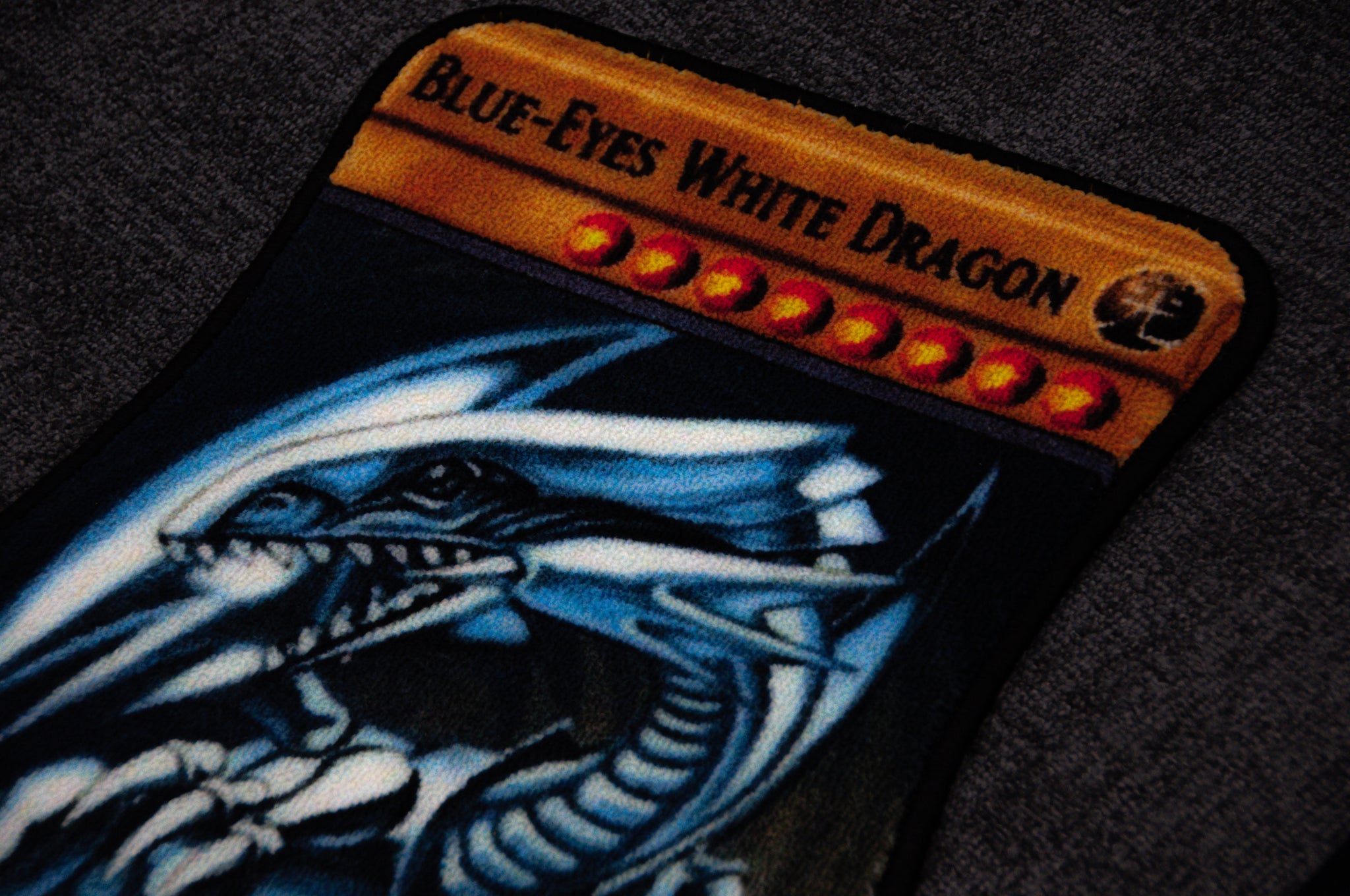 A close-up of the "Blue Eyes!!" floor mat by Incompletegl. The mat showcases a striking design of a blue and white dragon with piercing blue eyes, with its name prominently displayed at the top in bold letters. The slightly blurred background accentuates the detailed artwork and text on the product.