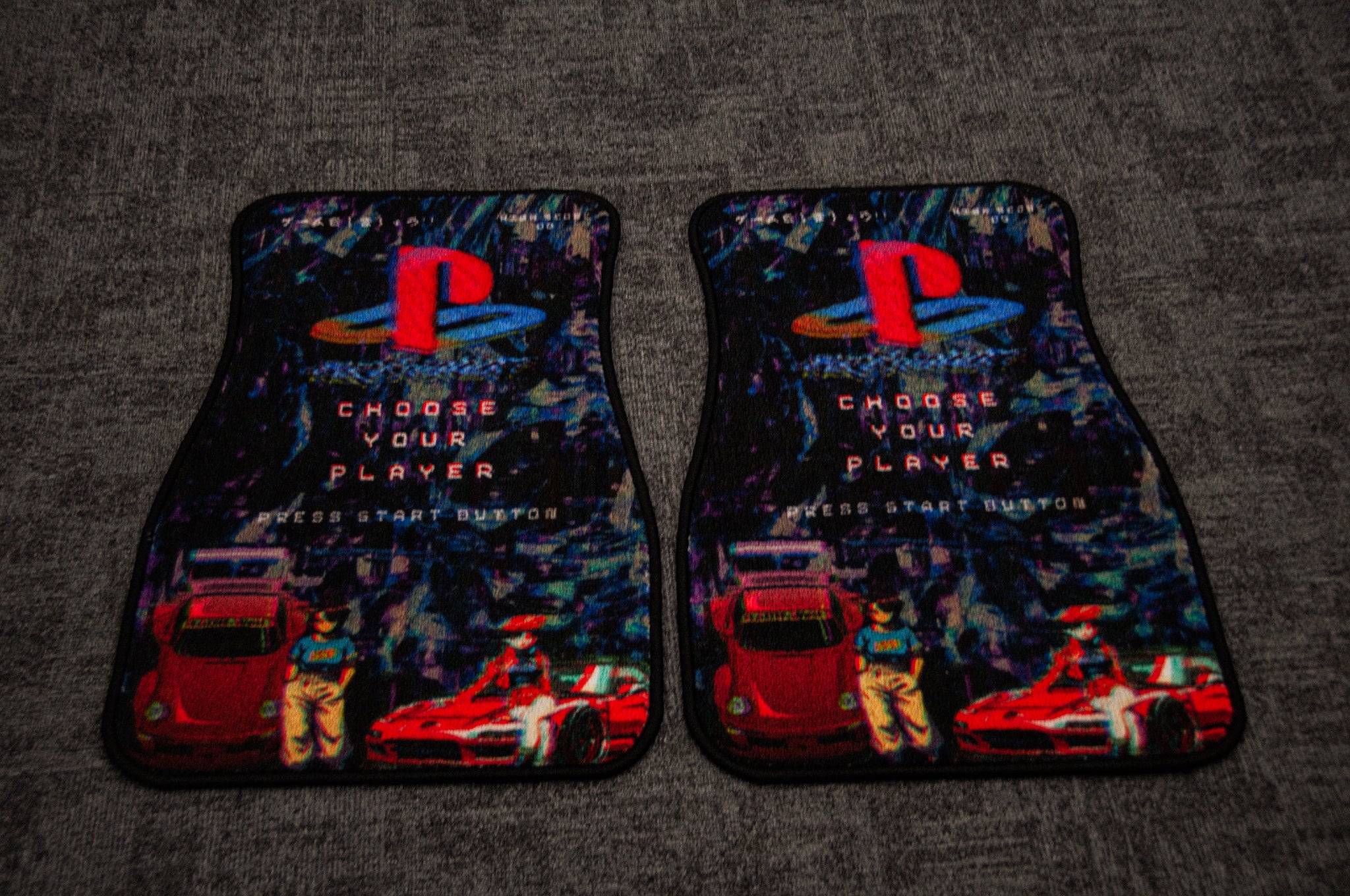 Introducing Retro Playstation! | Floor Mats by Incompletegl: Two floor mats featuring a vibrant design inspired by nostalgic PlayStation graphics. The mats prominently display the PlayStation logo at the top, with "Choose your player" and "Press start button" below, framed by colorful imagery of race cars and characters that exude strong gaming vibes.