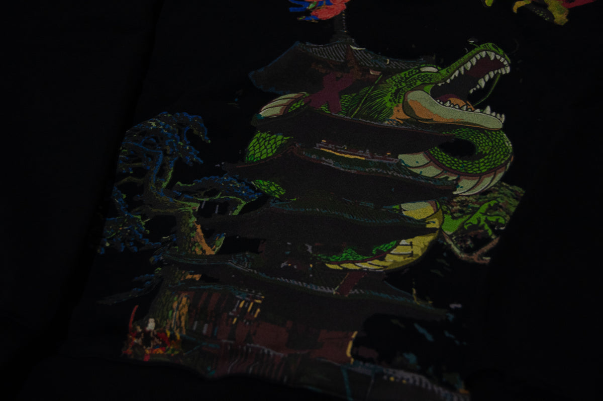 A detailed design on a dark fabric showcases a green dragon entwined around a traditional Asian pagoda. The dragon's mouth is open, displaying its teeth, and its body wraps tightly around the structure, blending with other artistic elements and colors— a true masterpiece titled "The Clash of Shenron x Ukiyo-e Style | Oversized Hoodie" by Incompletegl.
