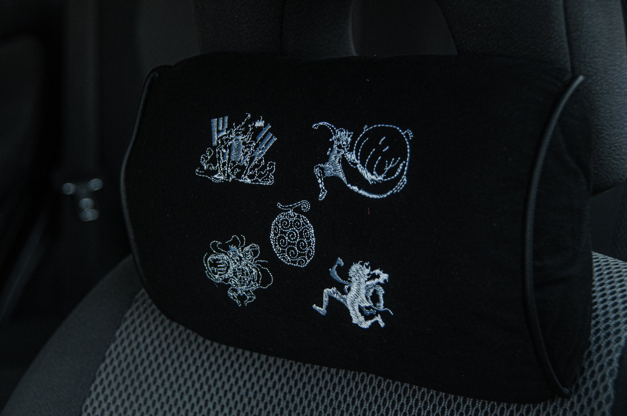 The Gear 5!!! Headrest Pillow by Incompletegl is a black car seat accessory inspired by Luffy's evolution. It boasts intricate white embroidery with abstract designs, capturing the adventurous spirit of One Piece and merging style with subtle flair.