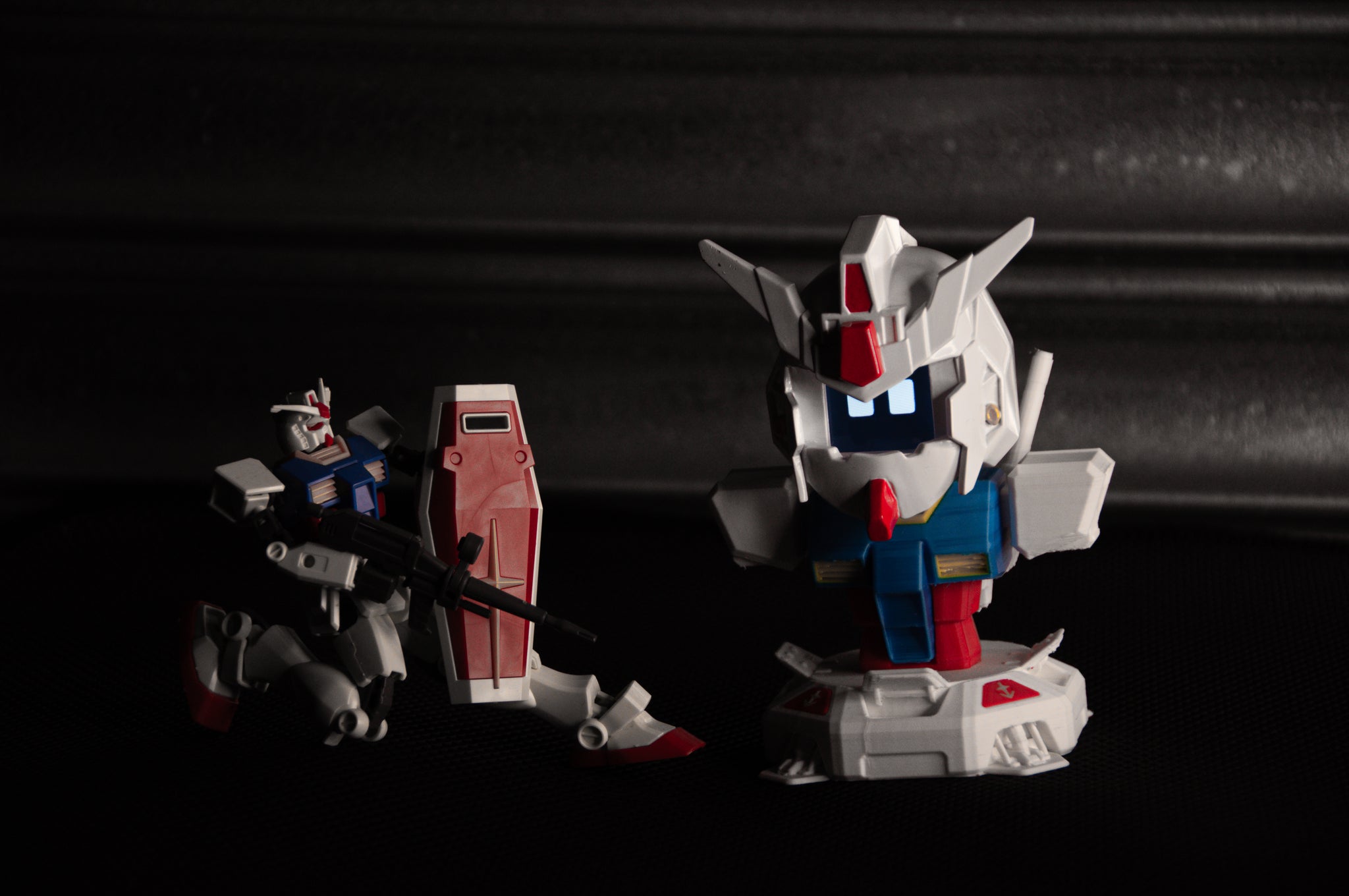 Displayed on a dark surface are two Gundam model figures from the "GENJI x RX78! | Limited Edition" collection by Incompletegl. One figure is an articulated RX-78 Gundam equipped with a weapon, while the other showcases an animated face with a large head and short limbs. Both models feature red, white, and blue accents that evoke the classic style of a beloved JDM driving companion.