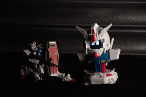 Displayed on a dark surface are two Gundam model figures from the "GENJI x RX78! | Limited Edition" collection by Incompletegl. One figure is an articulated RX-78 Gundam equipped with a weapon, while the other showcases an animated face with a large head and short limbs. Both models feature red, white, and blue accents that evoke the classic style of a beloved JDM driving companion.