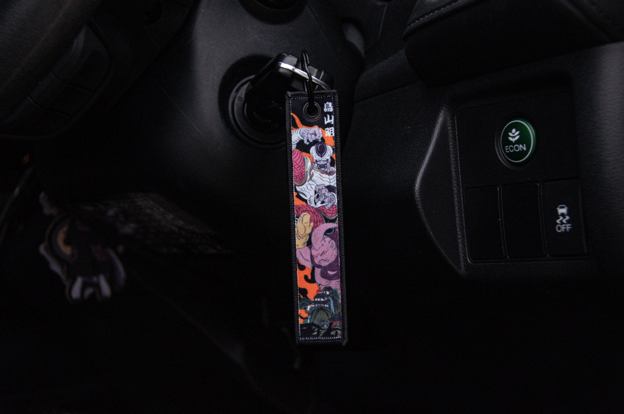 A DBZ x Ukiyo-e Style! Jet Tag from Incompletegl, adorned with vibrant illustrated characters, is attached to the car key as it is inserted into the ignition, adding an artistic flair. The dashboard contains buttons, including a green "Econ" button.