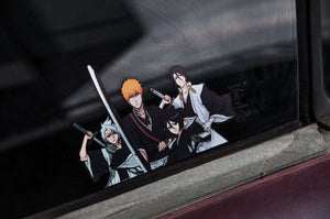 The Holographic Peeker Decal by Incompletegl displays four anime characters in martial arts attire, each holding swords and striking serious poses. One of the featured characters is Ichigo from Bleach, emanating intensity. The holographic design also reflects light from the window, while the car's exterior has a slightly worn look.