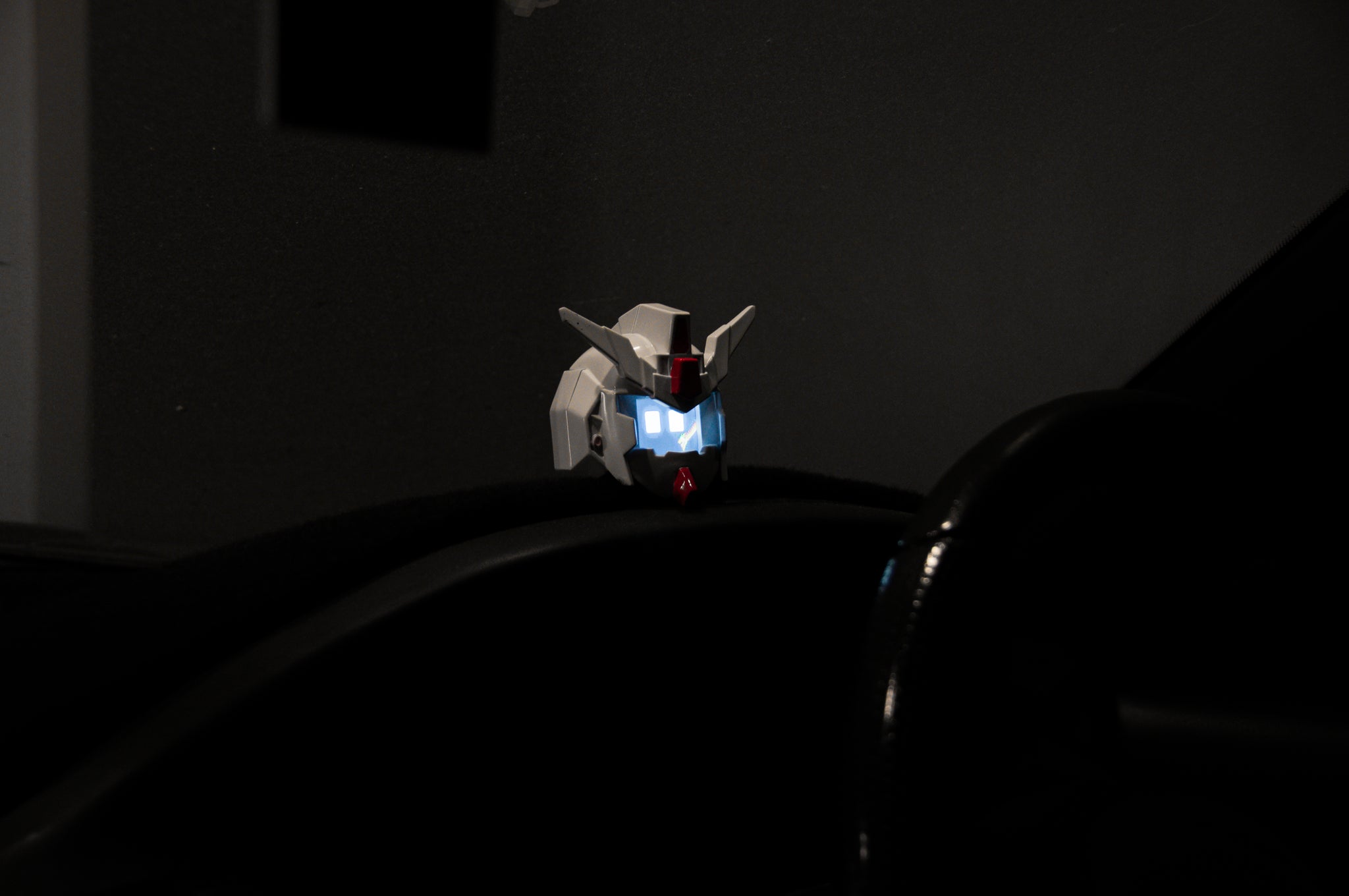 The GENJI x RX78! Limited Edition model head by Incompletegl makes an ideal JDM driving companion. With its illuminated eyes, it sits on a black surface in dim lighting, captivating all who see it with its futuristic gaze.