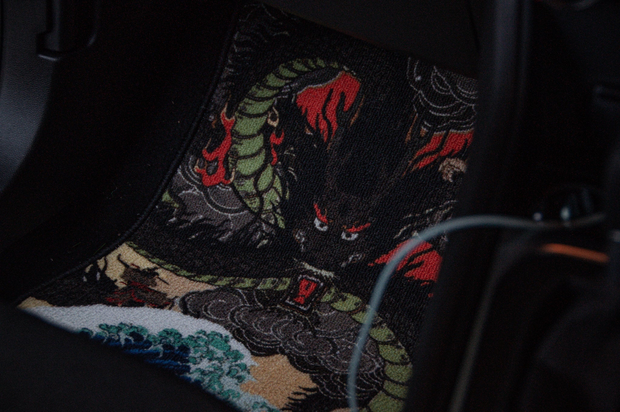 A car floor mat from Incompletegl's Dragon Ball Z x Ukiyo-e Style! collection, featuring an intricate, colorful design that depicts a fierce dragon with a red and green serpent-like body and a menacing face with red eyes, surrounded by flames, clouds, and waves. Reminiscent of Ukiyo-e art.