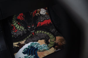 The Dragon Ball Z Super Pack! | Bundle Pack, an exclusive product from Incompletegl, features a car floor mat adorned with an intricate design of a fierce dragon. The dragon showcases a green body entwined with black and red flames, set against crashing ocean waves in the foreground. The predominantly dark background accentuates the vibrant colors of the dragon and waves, capturing the essence of Saiyan spirit in every detail.