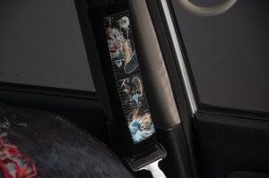 A close-up of the Incompletegl Luffy x Kaido!! seatbelt cushion showcases its artistic anime-themed design. This vibrant One Piece decorative piece enhances the vehicle's interior, featuring colorful characters and abstract motifs against the backdrop of the seat and door frame.