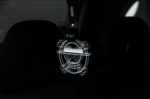 The Straw Hat! (Jolly Roger) | Tsurikawa! by Incompletegl is a transparent pendant featuring a cartoon skull with a straw hat and crossbones, elegantly dangling from a tsurikawa strap in the car interior, with the dark background hinting at the car seat for an edgy touch.