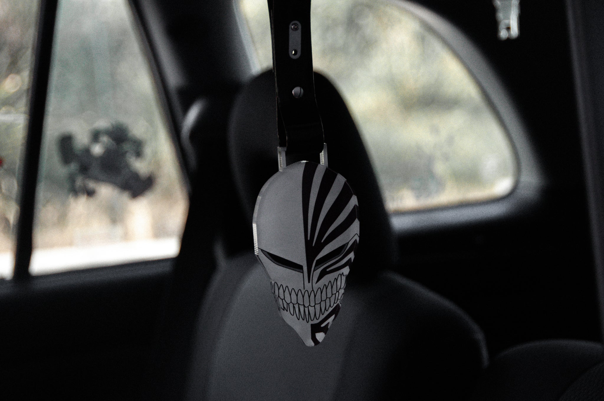 A Hollow Form | Tsurikawa from Incompletegl, featuring black and white striped, jagged patterns inspired by Ichigo Kurosaki, hangs from the rearview mirror inside a car as the seats and windows blur in the background.