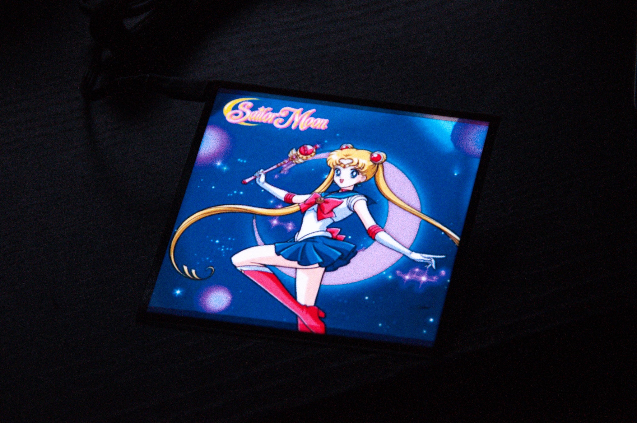 An image of the Sailor Moon! Glow Panel, a square display from Incompletegl, featuring the famous anime character Sailor Moon posed in a fighting stance against a cosmic background with the text "Sailor Moon" at the top. She is dressed in her iconic sailor outfit and holding a magical staff. This panel is an ideal JDM accessory for fans and collectors alike.