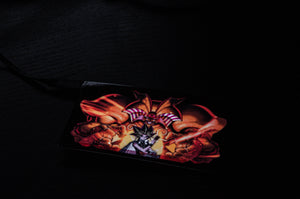 In a dark image, a card showcasing colorful, detailed artwork of a winged, horned creature looming over an armored character is prominently displayed. Reminiscent of the Yu-Gi-Oh! series, the Exodia! | Glow Panel by Incompletegl is attached to a black strap, evoking the intensity of Yugi x Exodia duels.