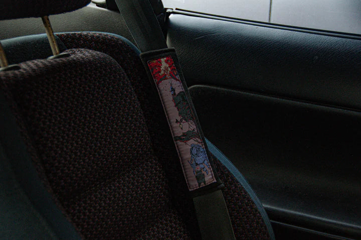 Naruto-themed car seat with a patterned seatbelt cover from the Naruto Mystery Pack! Anime Bundle by Incompletegl. The car's dim interior highlights textured fabric seats, allowing minimal light to enter through the window.