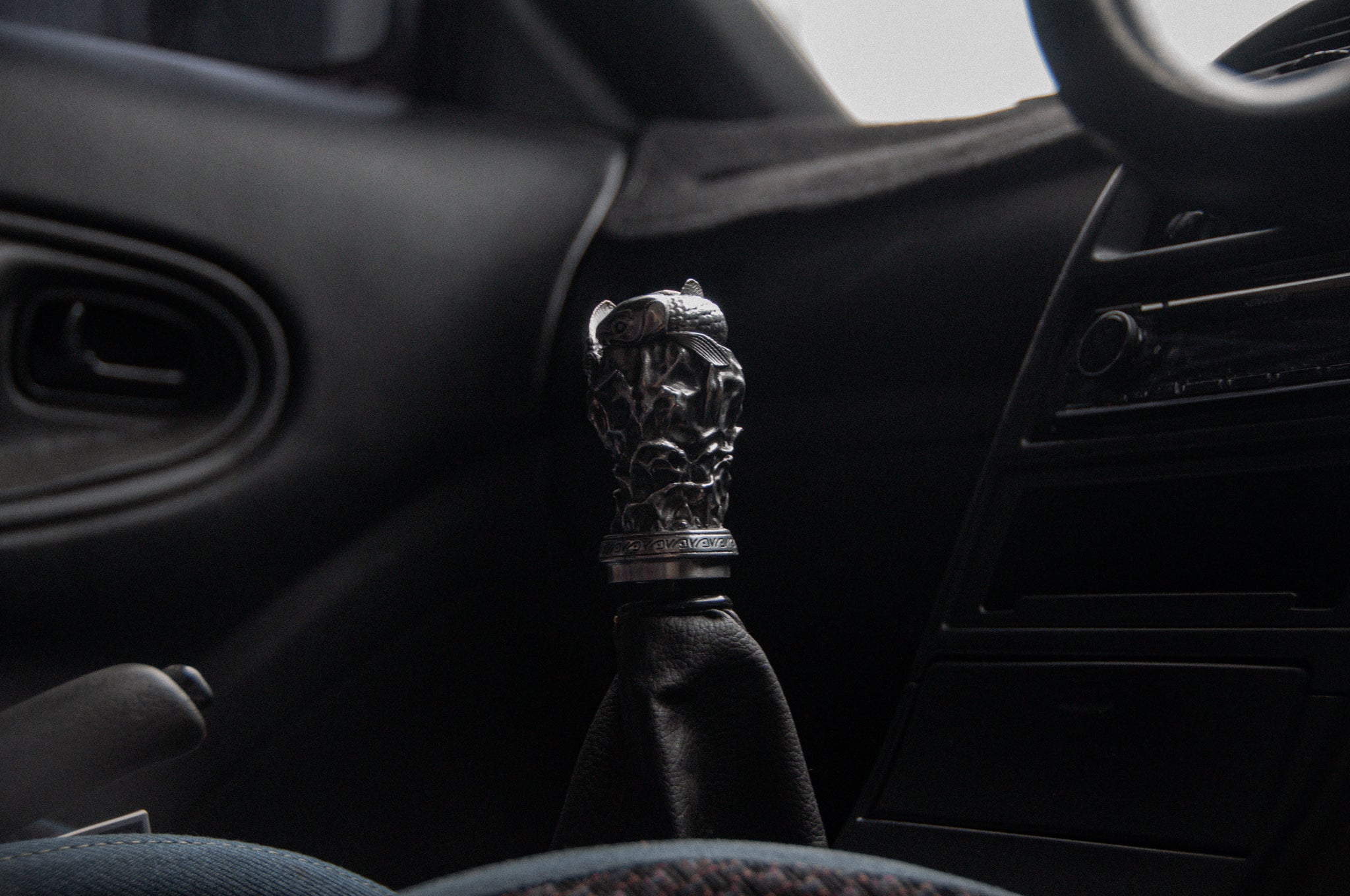 Close-up of a car gear shift showcasing the Twin Koi Fish | Artisan Shift Knob by Incompletegl. The dimly lit interior reveals part of the steering wheel and dashboard, emphasizing its unique handcrafted JDM style.