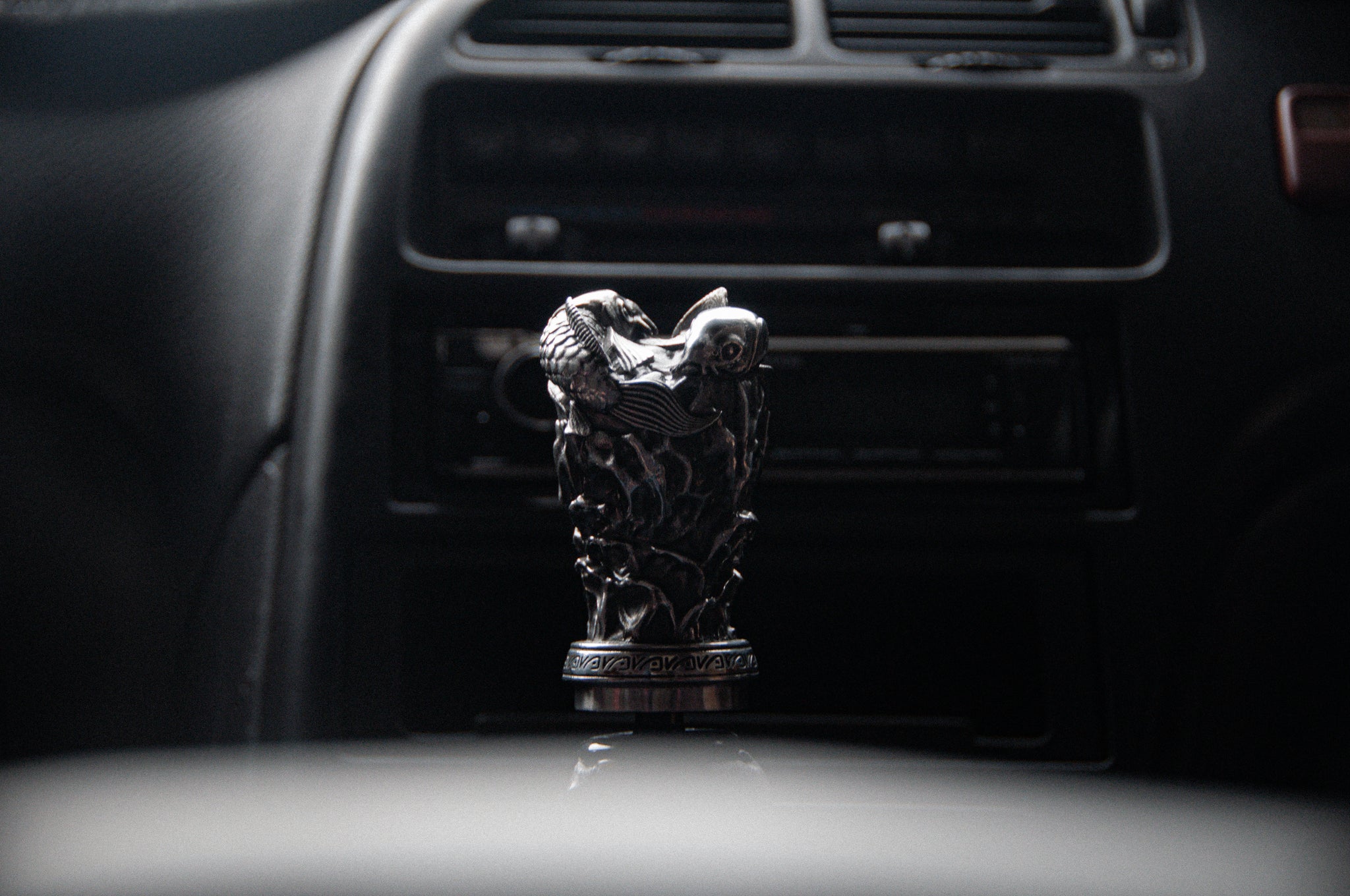 A close-up of a car interior highlights an Incompletegl Twin Koi Fish | Artisan Shift Knob, reflecting Japanese heritage with intricate koi detailing. The dashboard is slightly blurred in the background, emphasizing the handmade craftsmanship.