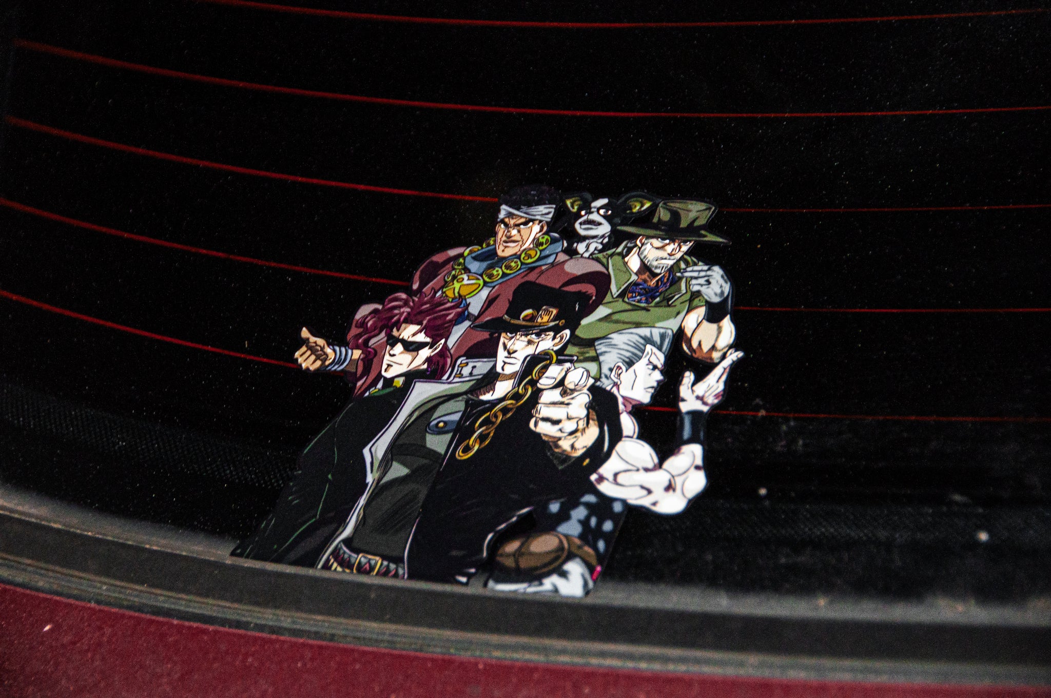 The JoJo Bizarre Adventure! Holographic Peeker Decal by Incompletegl showcases five characters from the anime "JoJo's Bizarre Adventure" on a JDM car window. The characters are depicted in dynamic poses and stylish outfits, with red lines from the car's defroster visible in the background.