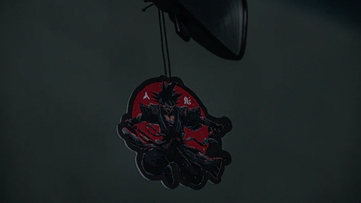The Dragon Ball Z Super Pack! Bundle by Incompletegl includes a hanging car air freshener shaped like a warrior character in black armor with red accents. The dynamic warrior, holding a sword while crouching, is set against a red circular background. Perfect for fans of Dragon Ball Z, it easily attaches to the rearview mirror with a black string.