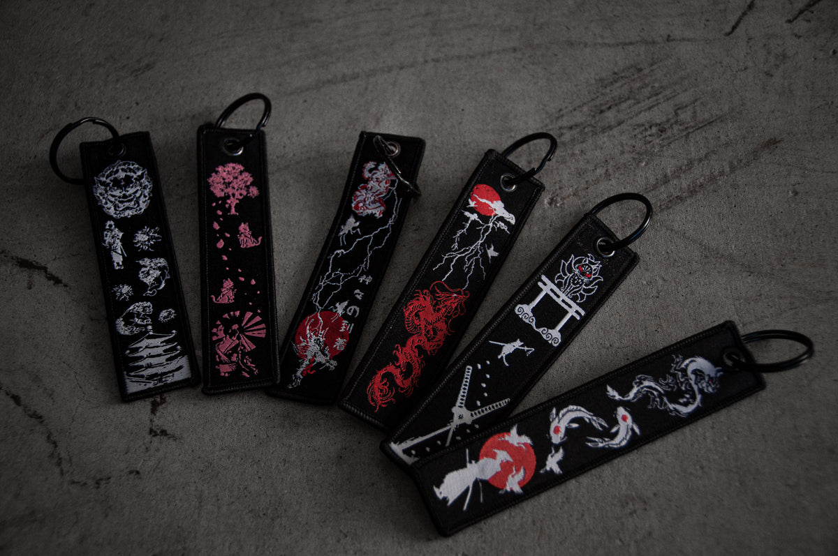 A set of three Jet Tag keychains laid on a grey surface. Each features unique designs with intricate and colorful illustrations, including dragons, cherry blossoms, abstract patterns, and other decorative elements against dark backgrounds. Don't miss the discount on this remarkable "Jet Tag Mega Pack!" by Incompletegl!