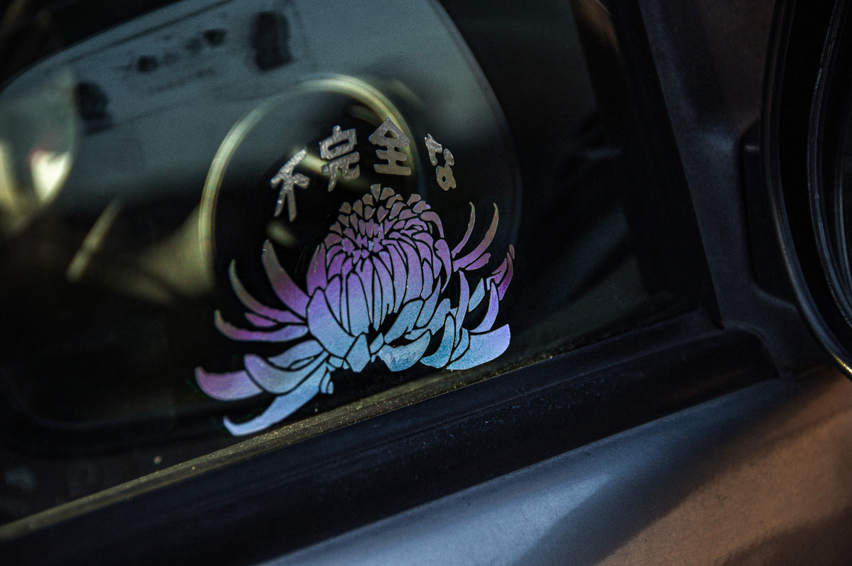 An Incompletegl T-shirt showcases a vibrant decal of a blooming chrysanthemum with Japanese characters above, embodying the gradient effect that shifts through shades of purple, pink, and blue—reminiscent of the vibrant patterns often seen on a traditional geisha's kimono.